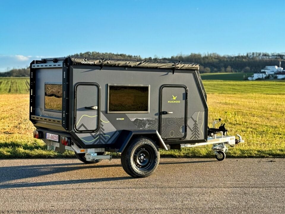 Ein kompakter, schwarzer Camper-Trailer im Teardrop-Stil – ein echtes Allround-Talent für Abenteuerlustige. Mit seinen großen Fenstern bietet dieser Offroad-Camper nicht nur eine hervorragende Aussicht in die Natur, sondern auch Komfort und Flexibilität unterwegs. Geparkt auf einer Landstraße, umgeben von Feldern und fernen Bäumen unter klarem, blauen Himmel, steht dieser Pickup Camper sinnbildlich für grenzenlose Freiheit beim Reisen. Perfekt für alle, die einen individuellen Custom Camper suchen und mit ihrem Pickup Truck unabhängig die schönsten Orte entdecken möchten!. Travelboxx - Pickup Wohnkabinen