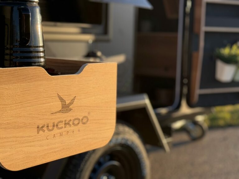 Nahaufnahme einer Holzoberfläche mit dem Schriftzug „Kuckoo Camper“, angebracht an der Seite eines Offroad-Campers oder Pickup Campers. Auf der Oberfläche steht eine schwarze Thermosflasche, und Sonnenlicht fällt auf dieses vielseitige Allround-Talent für grenzenlose Freiheit. Egal ob als Custom Camper für dein individuelles Abenteuer oder als robuster Pickup Camper – die hochwertige Verarbeitung macht jede Reise zum besonderen Erlebnis. Travelboxx - Pickup Wohnkabinen