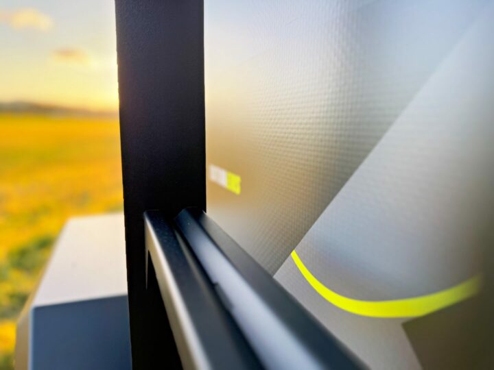 Nahaufnahme eines modernen Outdoor-Schilds mit einem eleganten, metallischen Rahmen und einer Grafik mit einer gelben, geschwungenen Linie – im Hintergrund ein unscharfes Bildfeld im Sonnenlicht. Dieses Motiv steht sinnbildlich für grenzenlose Freiheit und die Vielseitigkeit eines echten Allround-Talents – perfekt für alle, die auf der Suche nach einem Pickup Camper, Offroad Camper oder einer individuell angefertigten Custom Camper Lösung sind. Travelboxx - Pickup Wohnkabinen