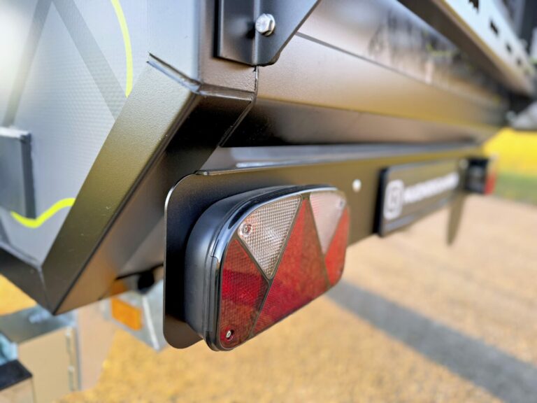 Nahaufnahme einer Heckecke eines Pickup Campers: Zu sehen sind ein rot-weißes Rücklicht, ein Teil des Nummernschilds sowie robuste Metalloberflächen mit Verschraubungen – das perfekte Beispiel für die hochwertige Verarbeitung und eine Langlebigkeit Offroad und Custom Campers. Mit Pickupboxx erleben Sie grenzenlose Freiheit bei Ihren Outdoor-Abenteuern – egal ob mit dem Pickup Camper oder einem individuell ausgestatteten Offroad Camper. Travelboxx - Pickup Wohnkabinen