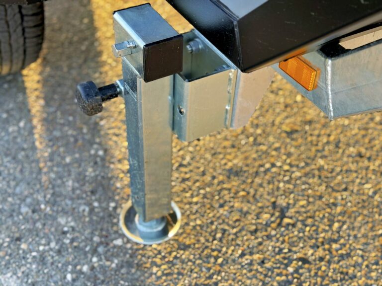 Nahaufnahme eines stabilen Metall-Stützfußes eines Offroad-Campers auf Asphalt – mit sichtbarem, schwarzem Verstellknopf und orangefarbenem Reflektor. Das Sonnenlicht hebt die Struktur des Bodens hervor. Dieses Allround-Talent ist ideal für grenzenlose Freiheit auf all deinen Pickup Camper- oder Custom Camper-Abenteuern und passt perfekt in deine Pickupboxx!. Travelboxx - Pickup Wohnkabinen